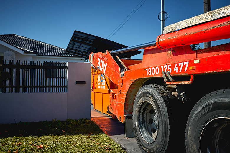 Photo of an ACE Skips & Waste truck with a skip bin in a home's driveway